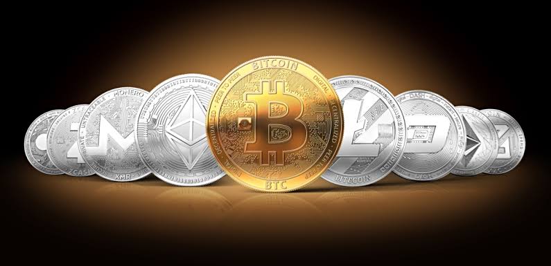 Gold Bitcoin and silver Ethereum coins resting on a laptop keyboard before a trading chart
